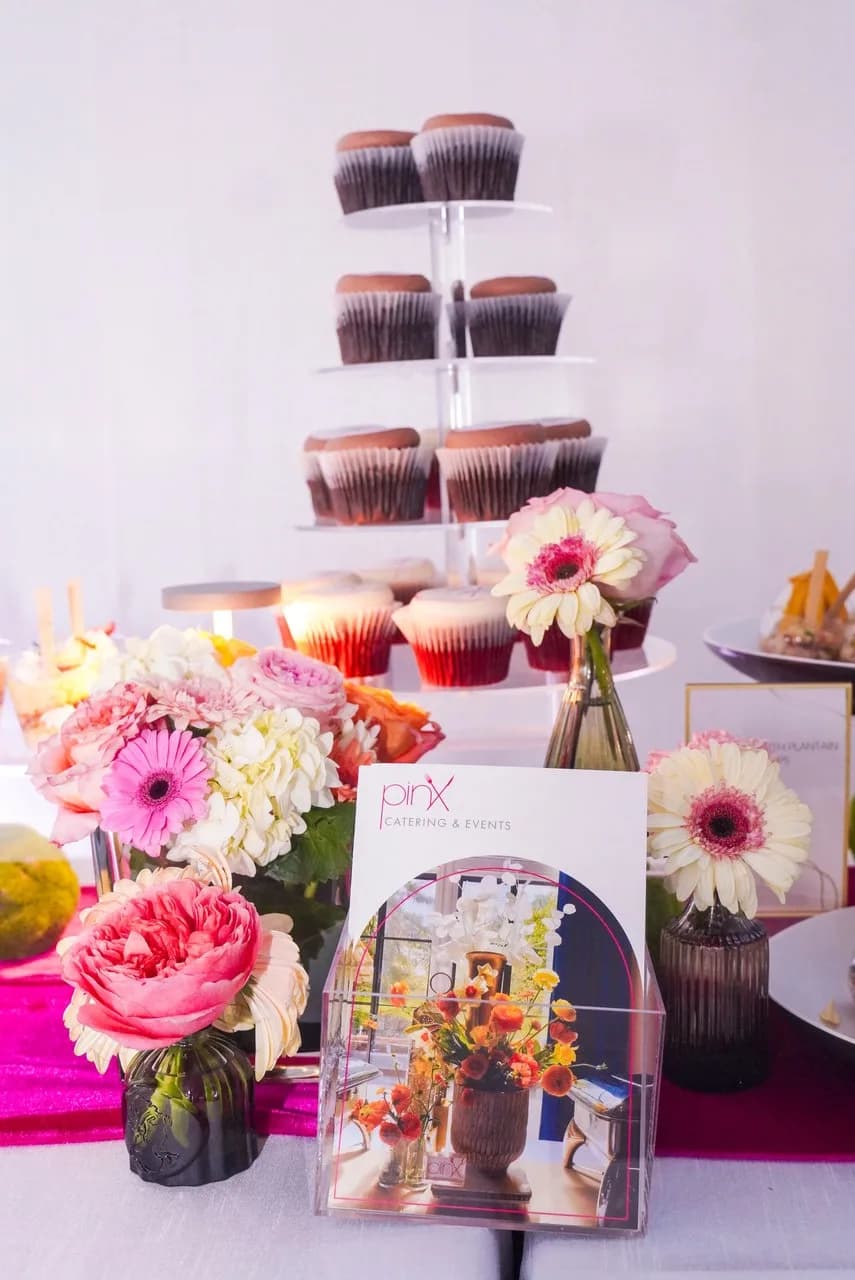 Tiered cupcake stand beside pink and cream floral arrangements and a Pinx Catering & Events card