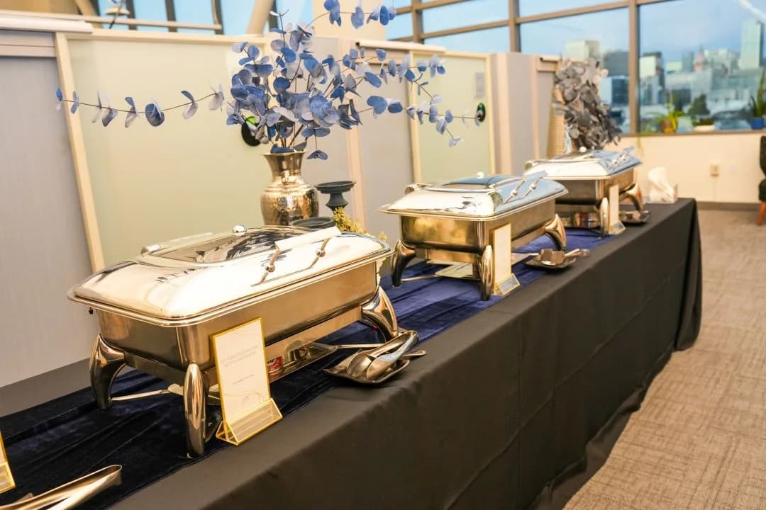 Three polished chafing dishes on a black-linen buffet with a navy runner and blue eucalyptus