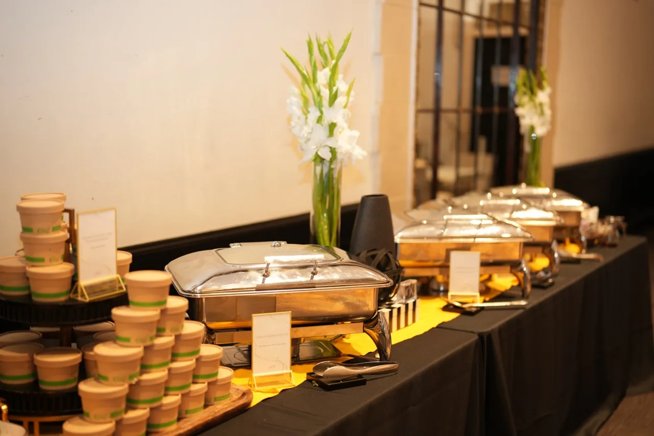 Long buffet line of gold chafing dishes with white gladiolus and stacked kraft soup cups