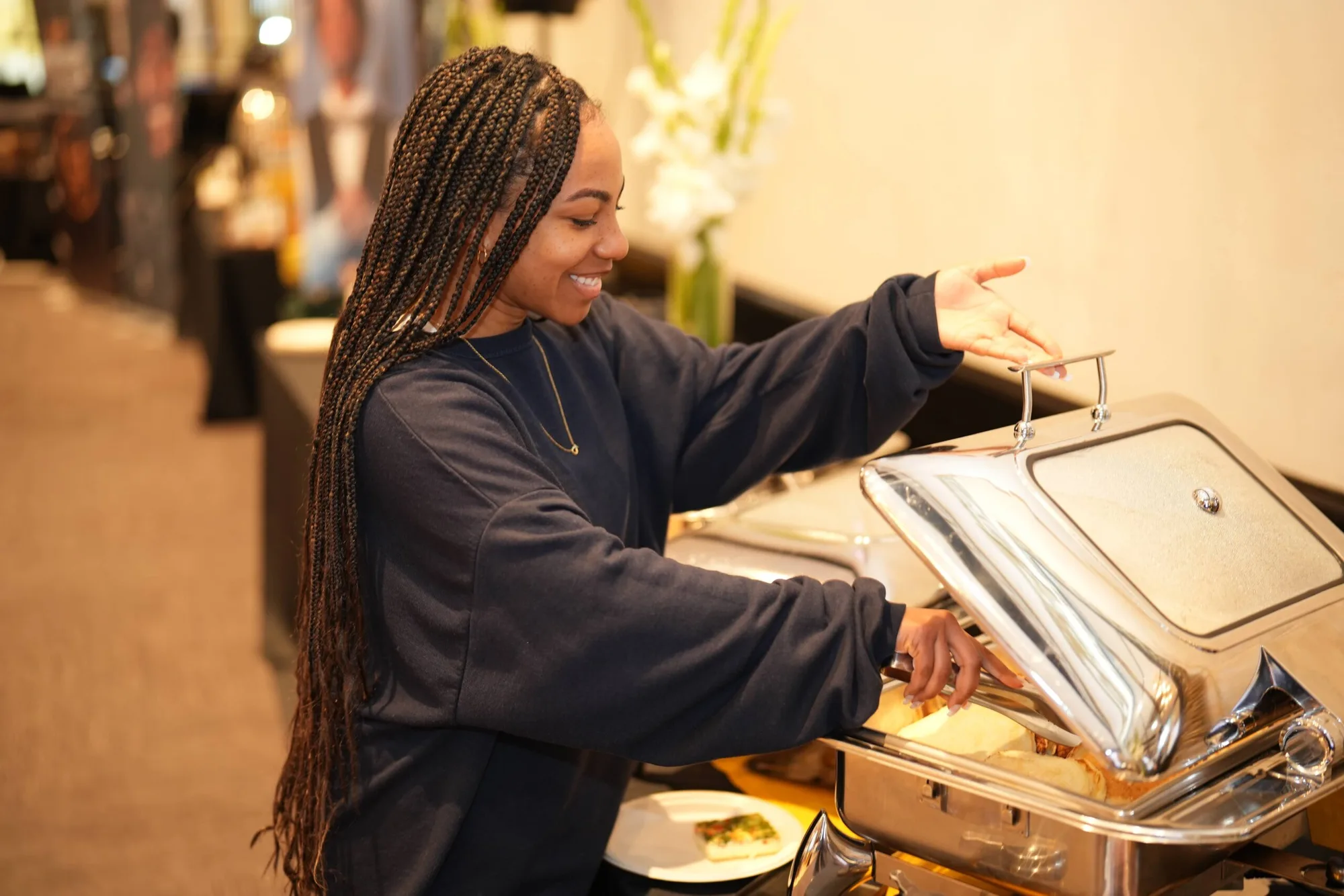 A Pinx team member lifting the lid of a chafing dish at a breakfast buffet set with white orchids