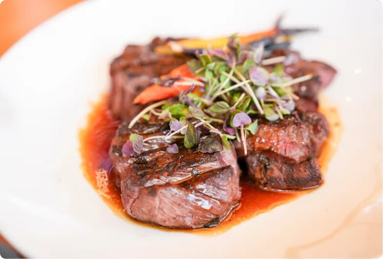 Plated steak medallions in jus with heirloom carrots and micro herbs