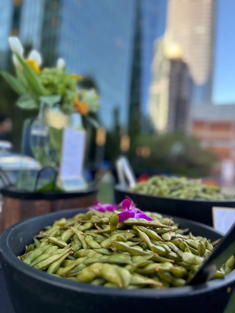 Bowls of edamame garnished with an orchid at a rooftop station, high-rise towers behind