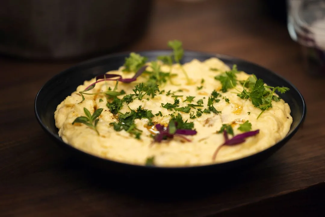A black bowl of creamy mashed potatoes finished with parsley, micro herbs and pickled red onion