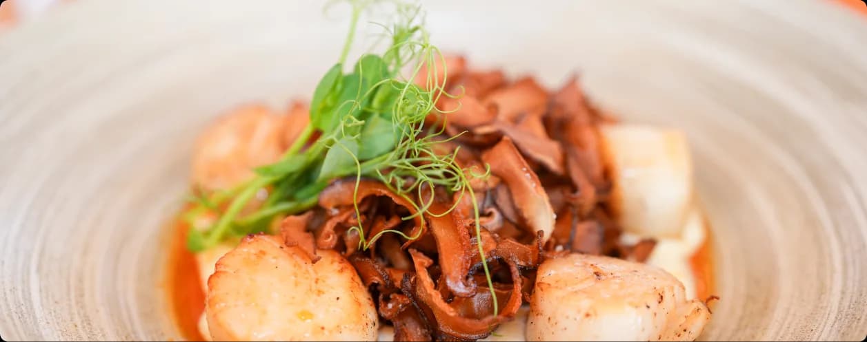 Seared scallops with crisped mushrooms and pea shoots plated on pale ceramic