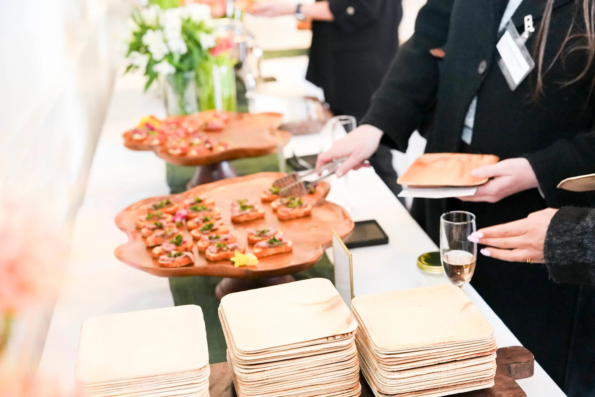 Guests serving themselves crostini from live-edge wooden platters beside stacks of wooden plates