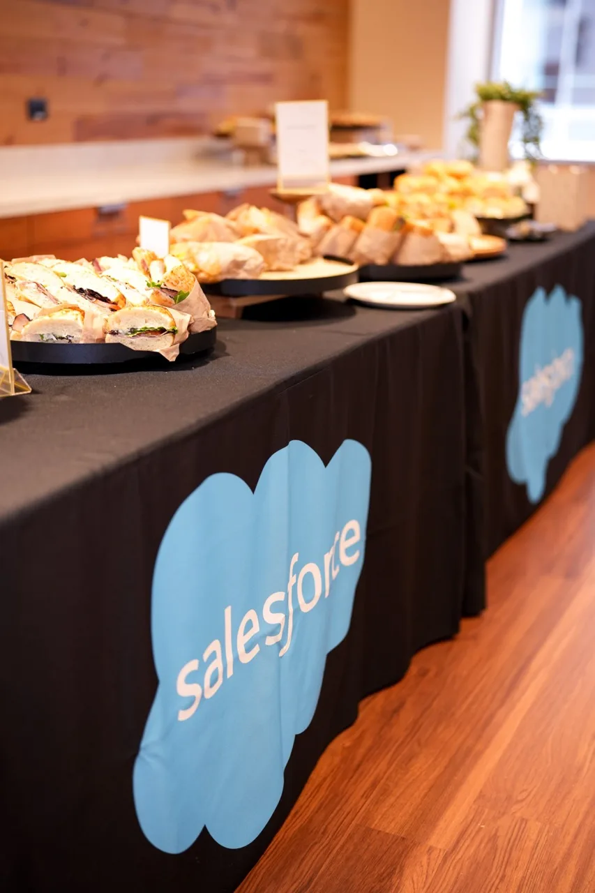 Sandwich and pastry buffet on a black table skirt printed with a client logo, in a wood-panelled office