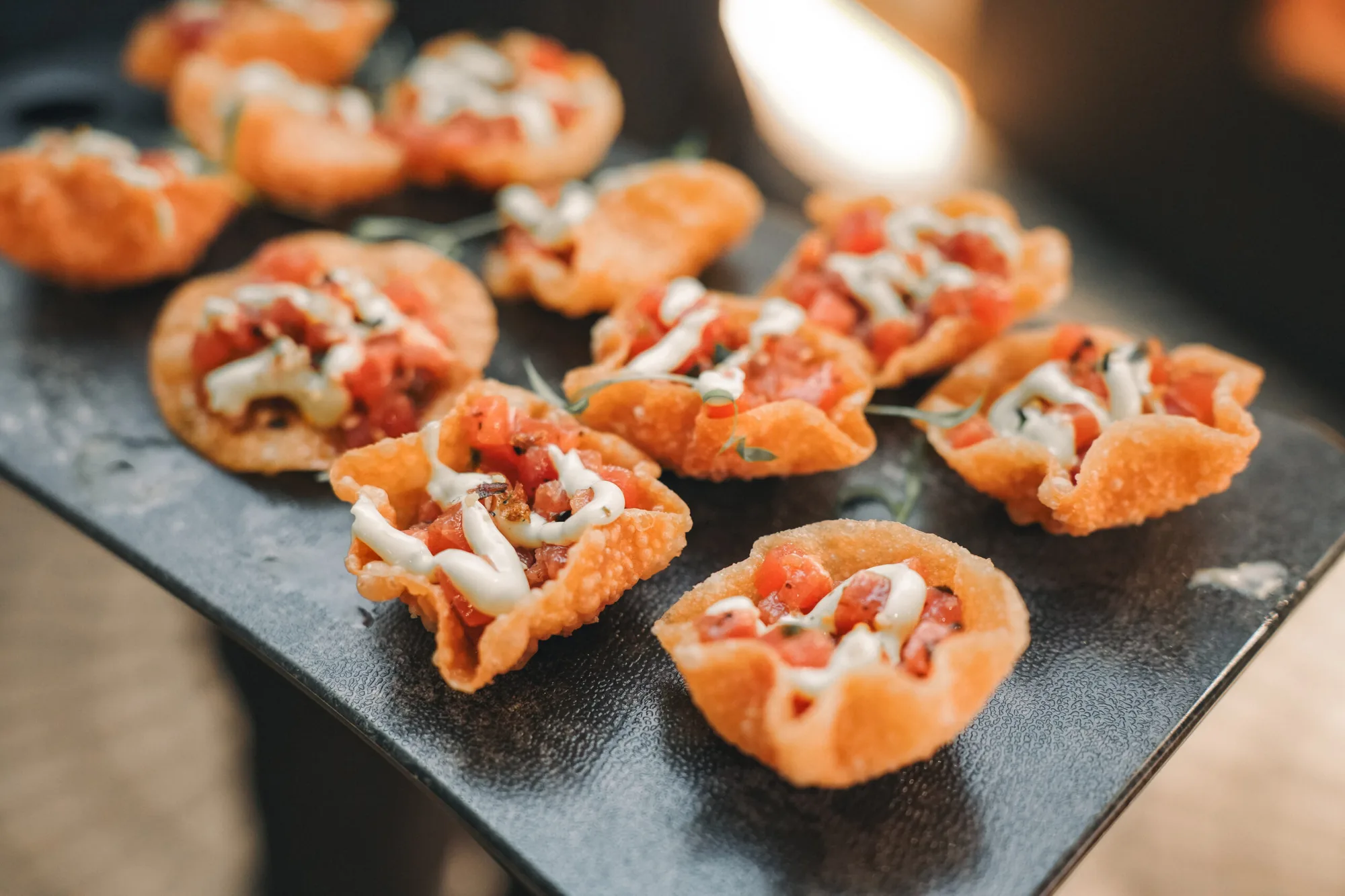 Crisp wonton cups filled with diced tomato and drizzled cream on a black slate board