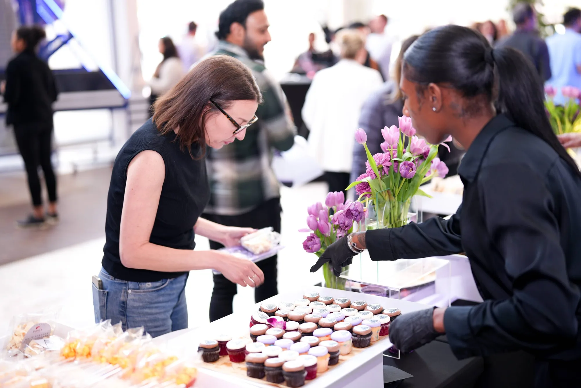A Pinx server tending a dessert display of logo-topped cupcakes as a guest makes a selection